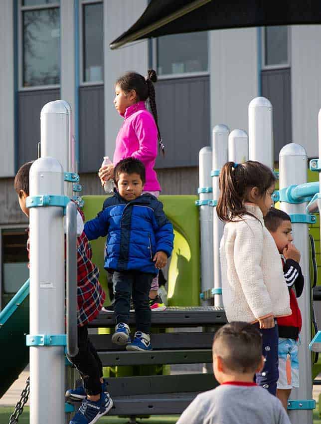 This image shows five children wearing bright colors and walking around on a white and blue playground at Vose Elementary.