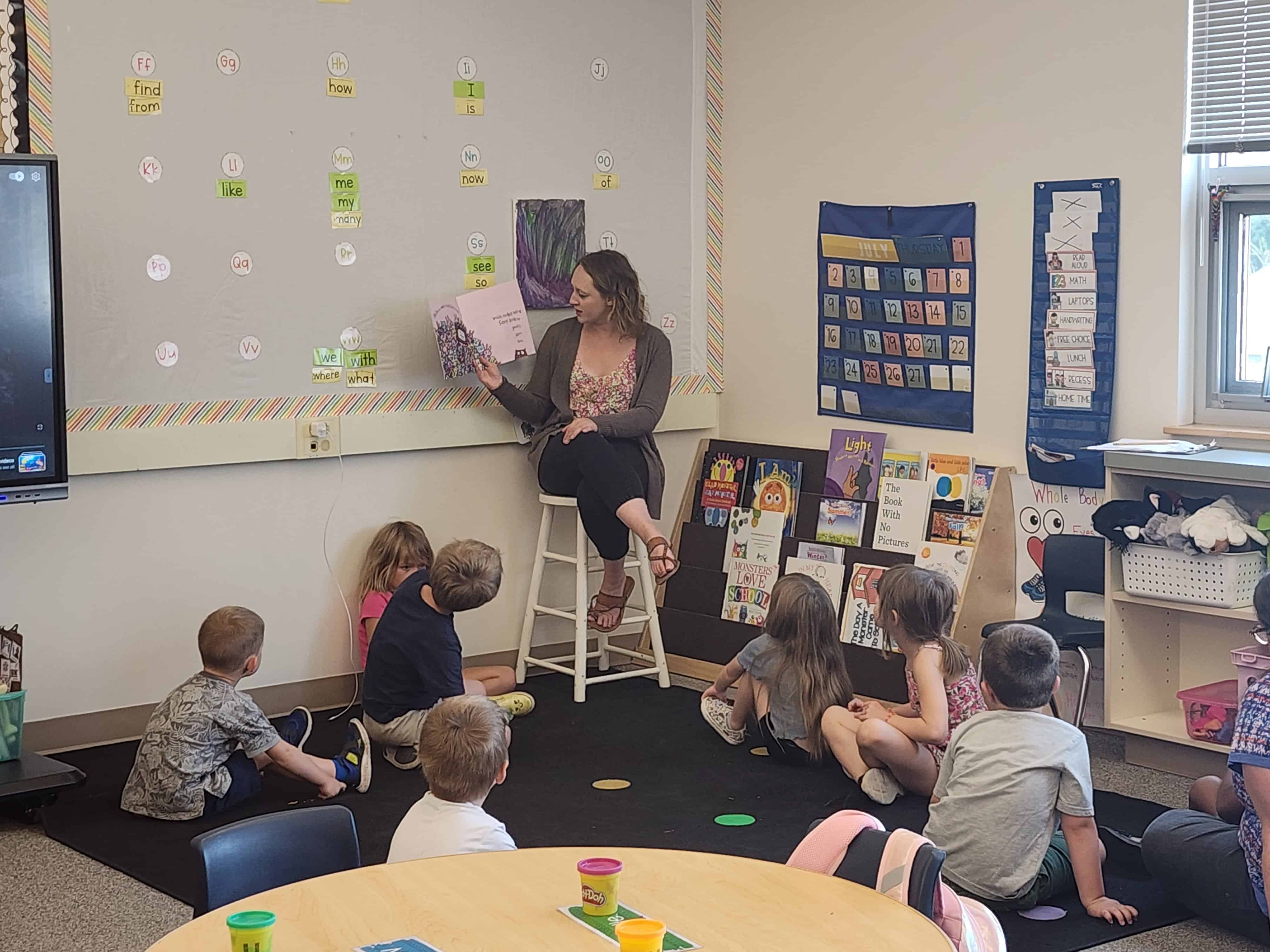 This image shows a group of young students learning from a teacher in a classroom at kinder camp.