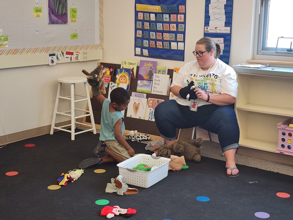 Kinder Camp teacher sits with a student in the classroom at Lewis and Clark Elementary.